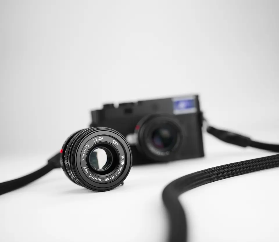 APO-Summicron-M 1:2/35 ASPH. vor der Leica M11-P – Festbrennweite mit Seilgurt auf weißem Grund