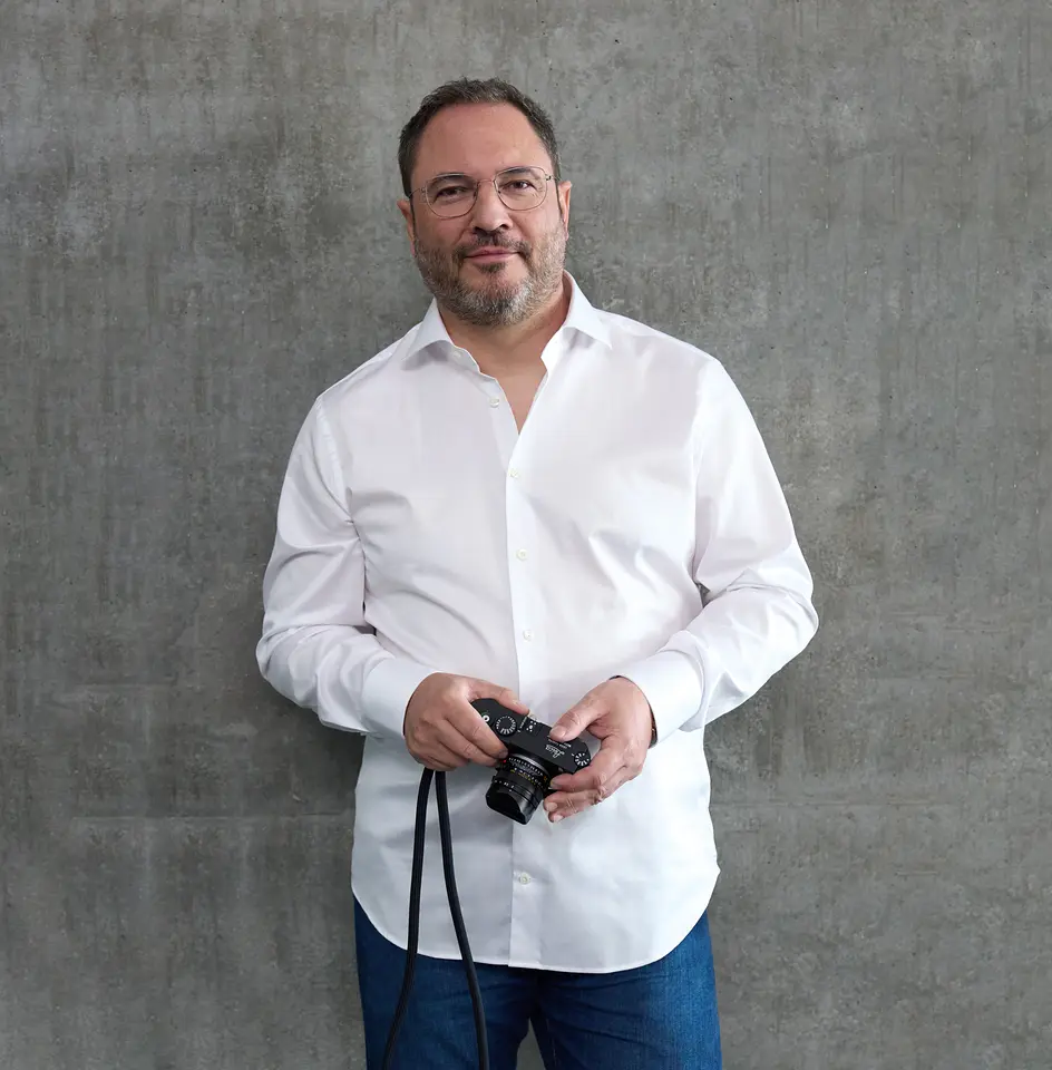 Mark Reinhardt, Inhaber von REINHARDT., Weinstadt – Porträt mit Leica-Kamera vor grauer Betonwand