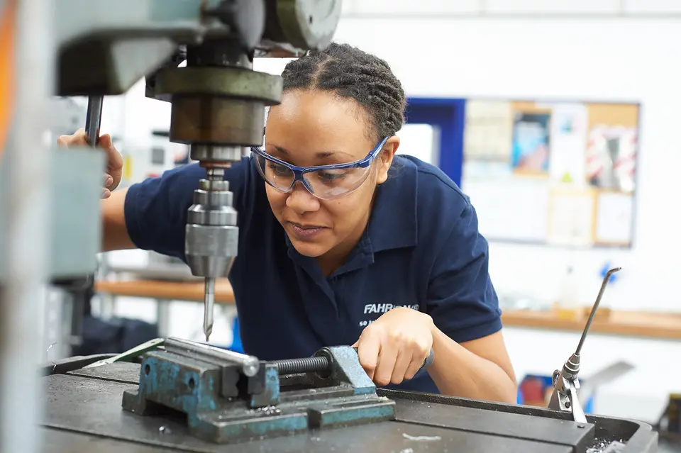 Ambiente de trabalho na Fahrion: colaboradora com óculos de proteção no engenho de furar de coluna na oficina